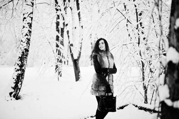 Elegance curly flicka i päls och handväska på snöiga skogen park — Stockfoto
