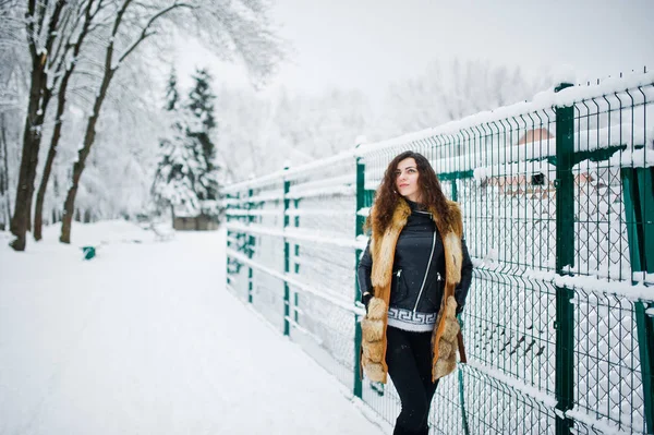 De gekrulde meisje elegantie in bontjas in het besneeuwde forest park op de winter. — Stockfoto