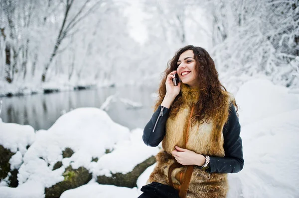 Elégance fille bouclée en manteau de fourrure avec téléphone portable à fores enneigées — Photo