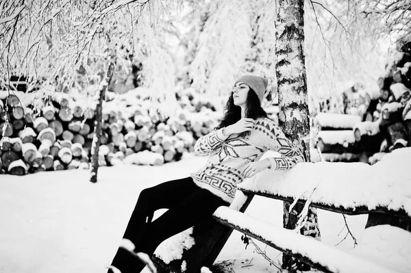 Menina encaracolado bonito em suéter e headwear sentado no banco na neve — Fotografia de Stock