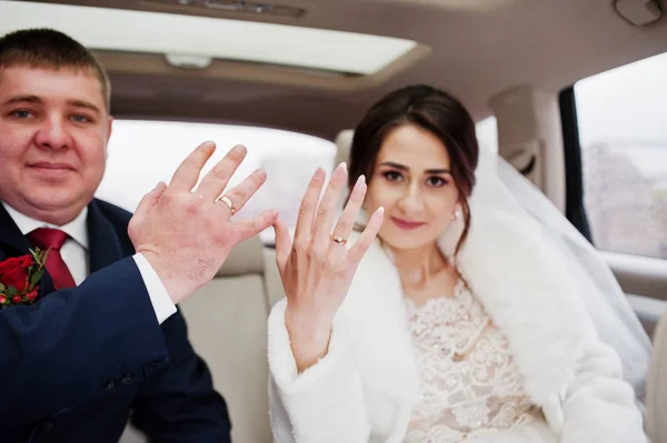 Couple de mariage assis dans la voiture et montrant leurs anneaux sur — Photo