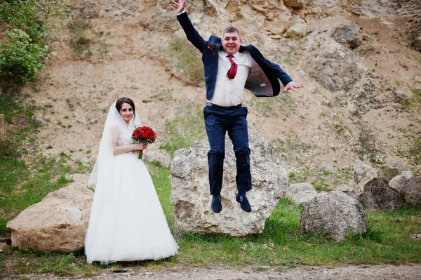 Noivo louco pulando de uma rocha e noiva olhando para ele em um casamento — Fotografia de Stock