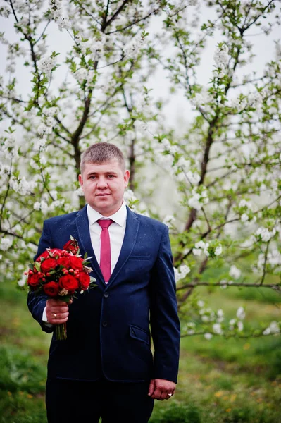 Portrait d'un marié tenant un bouquet dans un jardin fleuri . — Photo