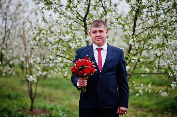 Portrait d'un marié tenant un bouquet dans un jardin fleuri . — Photo