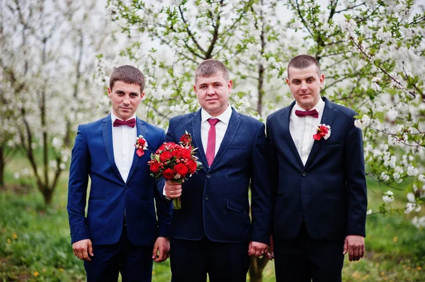 Pan młody trzyma bukiet i stoi z dwoma groomsmen w bloss — Zdjęcie stockowe