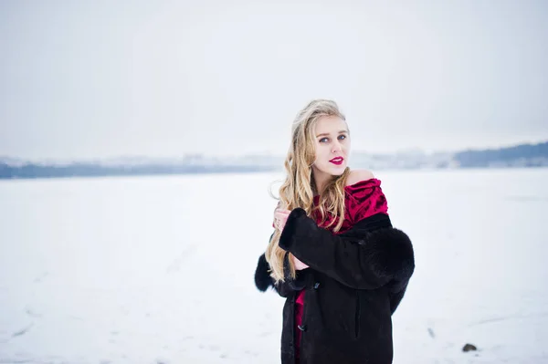 Élégante fille blonde en manteau de fourrure et robe de soirée rouge posée à — Photo