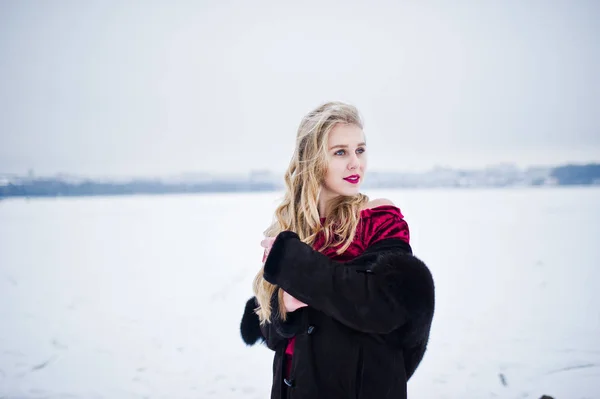 Élégante fille blonde en manteau de fourrure et robe de soirée rouge posée à — Photo