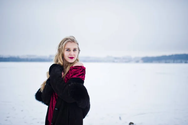 Élégante fille blonde en manteau de fourrure et robe de soirée rouge posée à — Photo