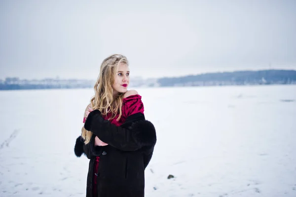 Élégante fille blonde en manteau de fourrure et robe de soirée rouge posée à — Photo