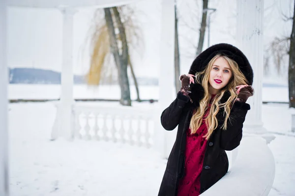 Élégante fille blonde en manteau de fourrure et robe de soirée rouge posée à — Photo