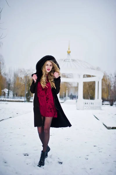 Élégante fille blonde en manteau de fourrure et robe de soirée rouge posée à — Photo