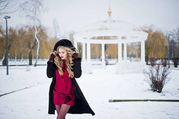 Élégante fille blonde en manteau de fourrure et robe de soirée rouge posée à — Photo