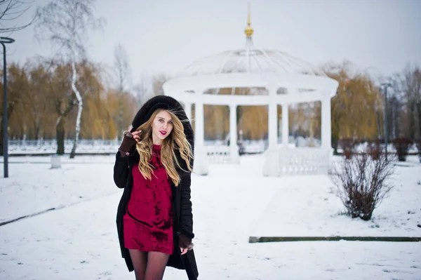 Élégante fille blonde en manteau de fourrure et robe de soirée rouge posée à — Photo