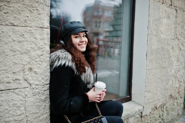 Curly mexican girl in leather cap and plastic cup of coffee at h — Stock Photo, Image