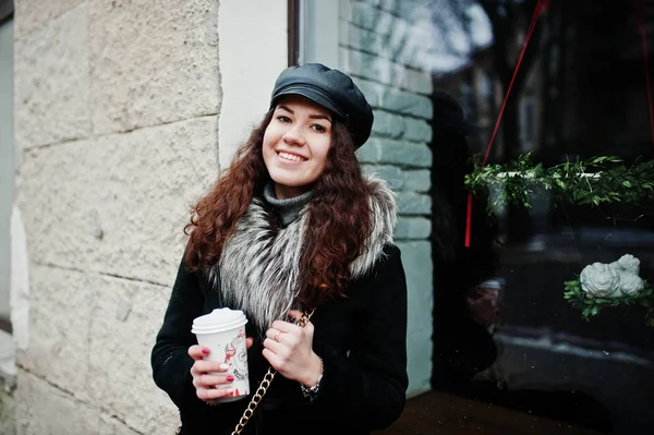 Curly mexican girl in leather cap and plastic cup of coffee at h — Stock Photo, Image