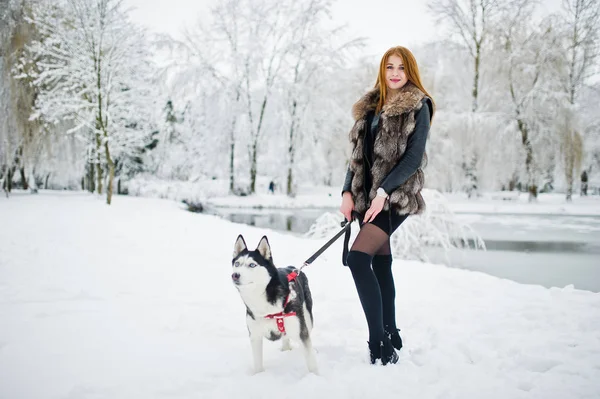 Rood harige meisje lopen in het park met husky hond op winterdag. — Stockfoto