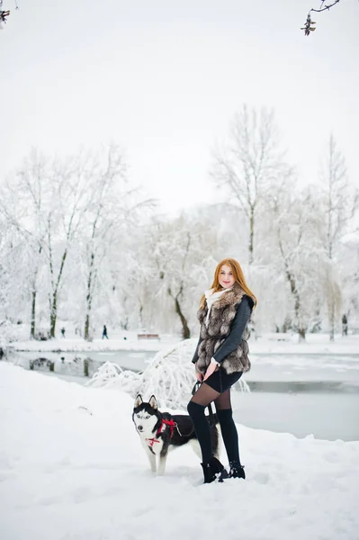 Menina de cabelos vermelhos andando no parque com cão husky no dia de inverno . — Fotografia de Stock