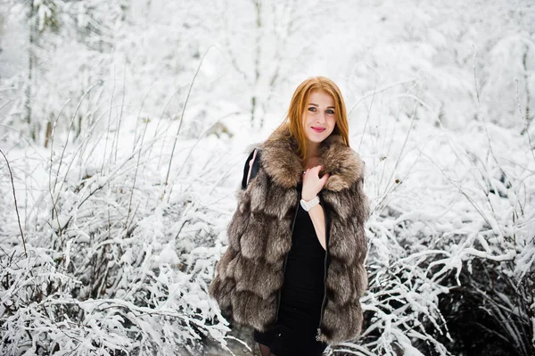 Fille aux cheveux rouges en manteau de fourrure marchant au parc enneigé d'hiver . — Photo