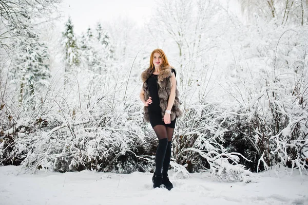 Rothaarige Mädchen im Pelzmantel spazieren im schneebedeckten Winterpark. — Stockfoto