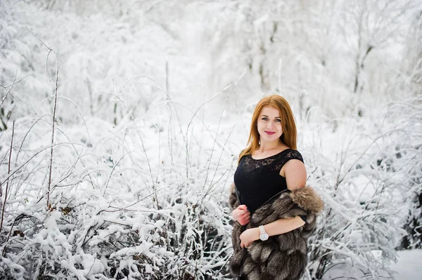 Fille aux cheveux rouges en manteau de fourrure marchant au parc enneigé d'hiver . — Photo