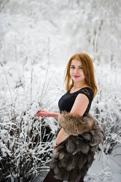 Menina de cabelos vermelhos em casaco de pele andando no parque nevado de inverno . — Fotografia de Stock