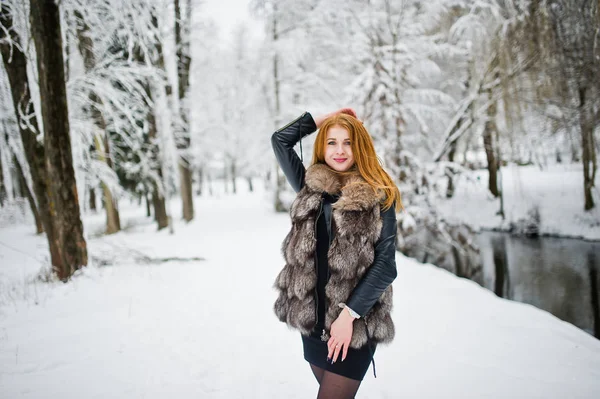 Fille aux cheveux rouges en manteau de fourrure marchant au parc enneigé d'hiver . — Photo