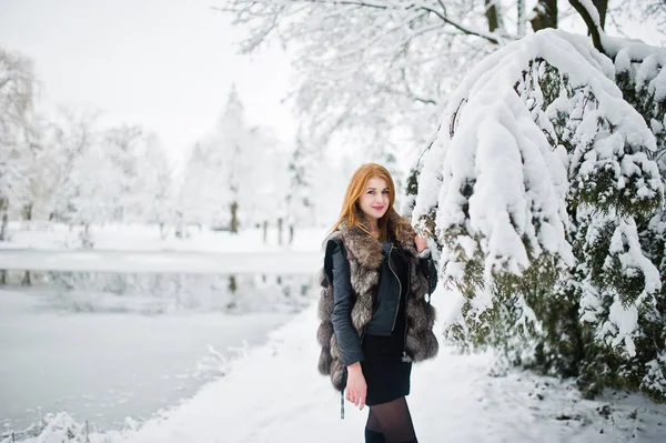 Menina de cabelos vermelhos em casaco de pele andando no parque nevado de inverno . — Fotografia de Stock