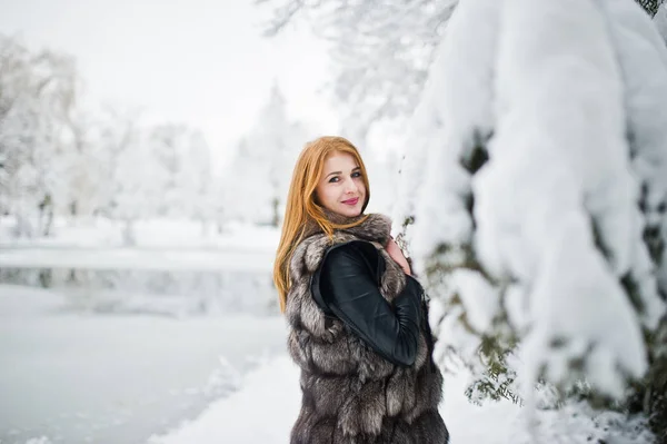 Rothaarige Mädchen im Pelzmantel spazieren im schneebedeckten Winterpark. — Stockfoto