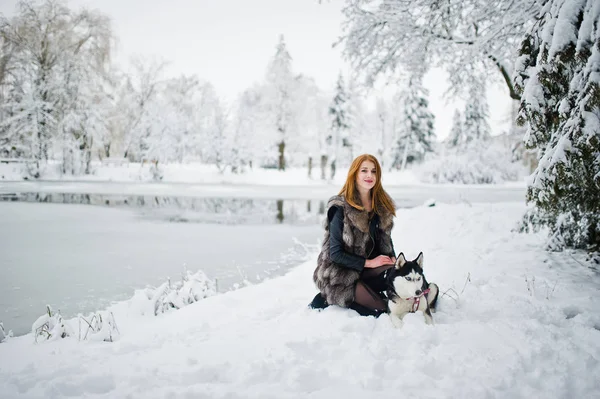 Menina de cabelos vermelhos andando no parque com cão husky no dia de inverno . — Fotografia de Stock