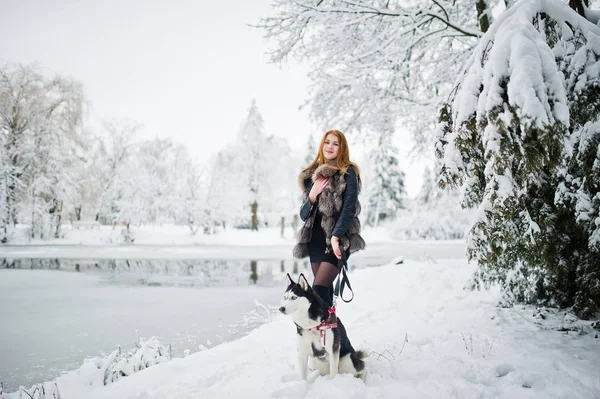 Menina de cabelos vermelhos andando no parque com cão husky no dia de inverno . — Fotografia de Stock