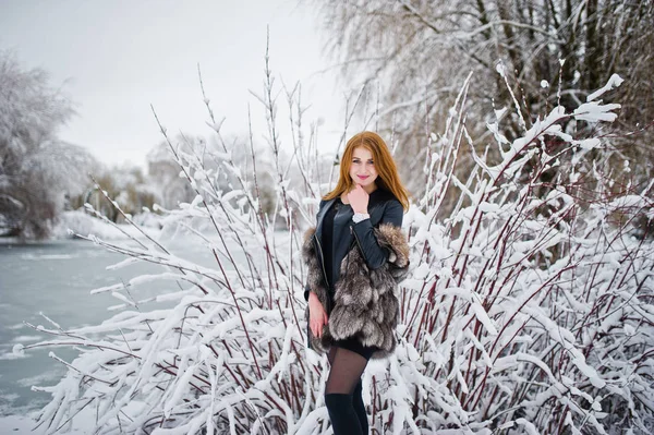 Fille aux cheveux rouges en manteau de fourrure marchant au parc enneigé d'hiver . — Photo