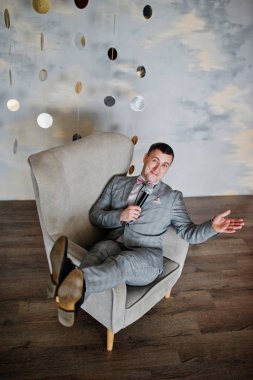 Sandalye backg üzerinde oturan mikrofon ile gri elbiseli yakışıklı adam