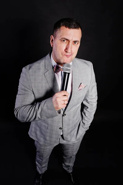 Handsome man in gray suit with microphone against black backgrou — Stock Photo, Image