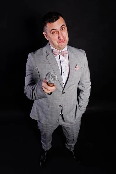 Homem bonito em terno cinza com microfone contra backgrou preto — Fotografia de Stock