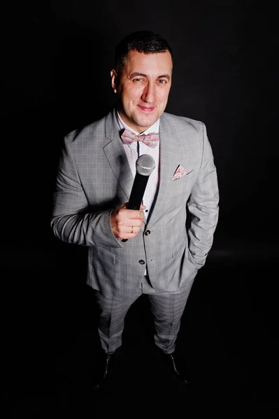 Siyah backgrou karşı mikrofon ile gri elbiseli yakışıklı adam — Stok fotoğraf
