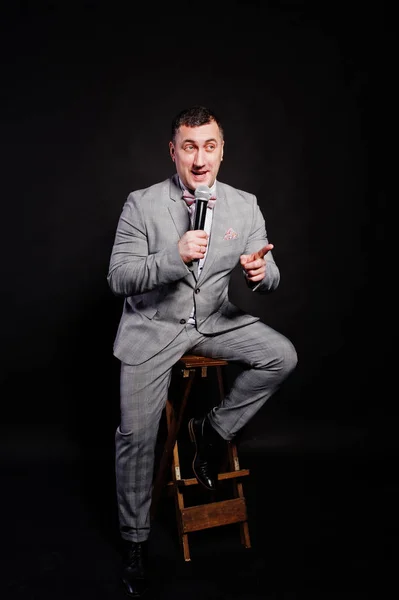 Handsome man in gray suit with microphone against black backgrou — Stock Photo, Image