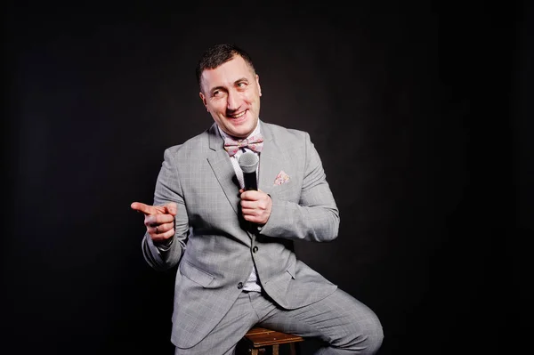 Handsome man in gray suit with microphone against black backgrou — Stock Photo, Image