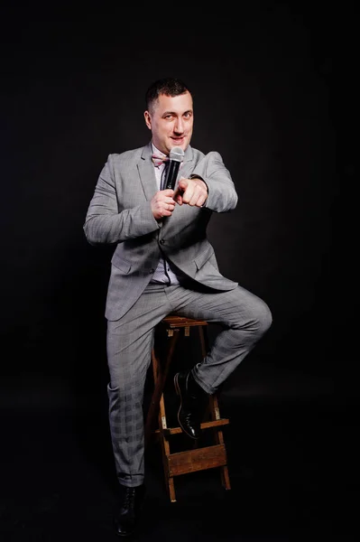 Pohledný muž v šedém obleku s mikrofonem proti černé poz — Stock fotografie