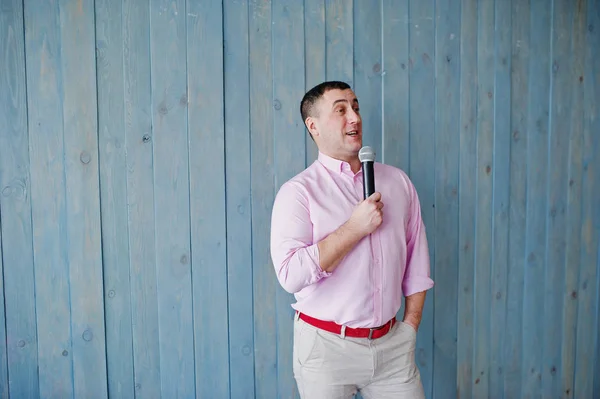 Knappe man in roze shirt met microfoon tegen blauwe houten w — Stockfoto