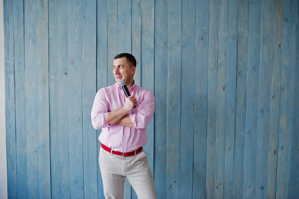 Handsome man in pink shirt with microphone against blue wooden w