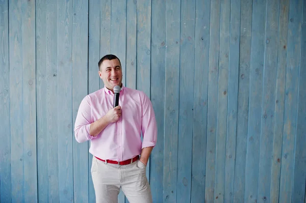 Όμορφος άνδρας στο ροζ πουκάμισο με μικρόφωνο εναντίον μπλε ξύλινο w — Φωτογραφία Αρχείου