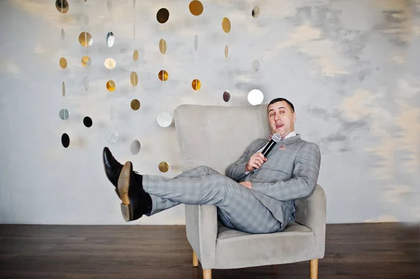 Knappe man in grijs pak met microfoon zittend op de stoel backg — Stockfoto