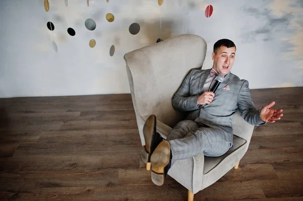 Knappe man in grijs pak met microfoon zittend op de stoel backg — Stockfoto