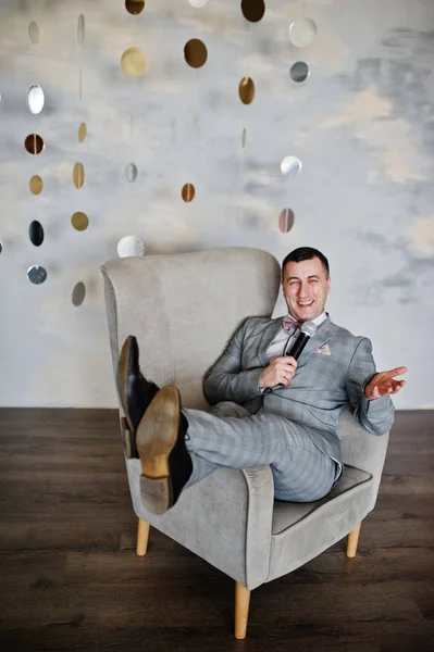 Handsome man in gray suit with microphone sitting on chair backg
