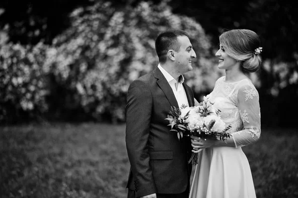 Giovane coppia innamorata contro i cespugli primaverili. Ragazza con bouquet . — Foto Stock