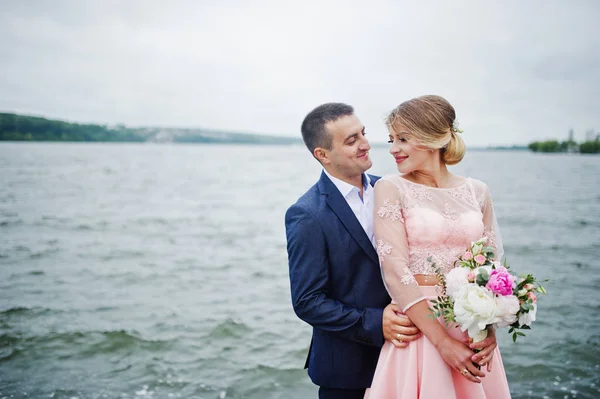 Casal jovem apaixonado contra lago. Menina com buquê . — Fotografia de Stock