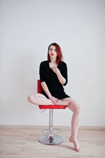 Rudowłosy dziewczyna na czarna sukienka tunika siedzi na przeciw czerwone krzesło — Zdjęcie stockowe