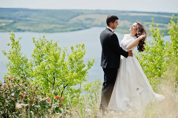 Wedding couple at breathtaking landscape with rock and lake. — Stock Photo, Image