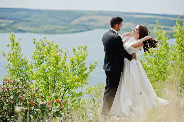 Wedding couple at breathtaking landscape with rock and lake. — Stock Photo, Image