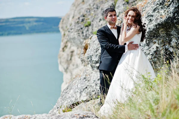 Wedding couple at breathtaking landscape with rock and lake. — Stock Photo, Image